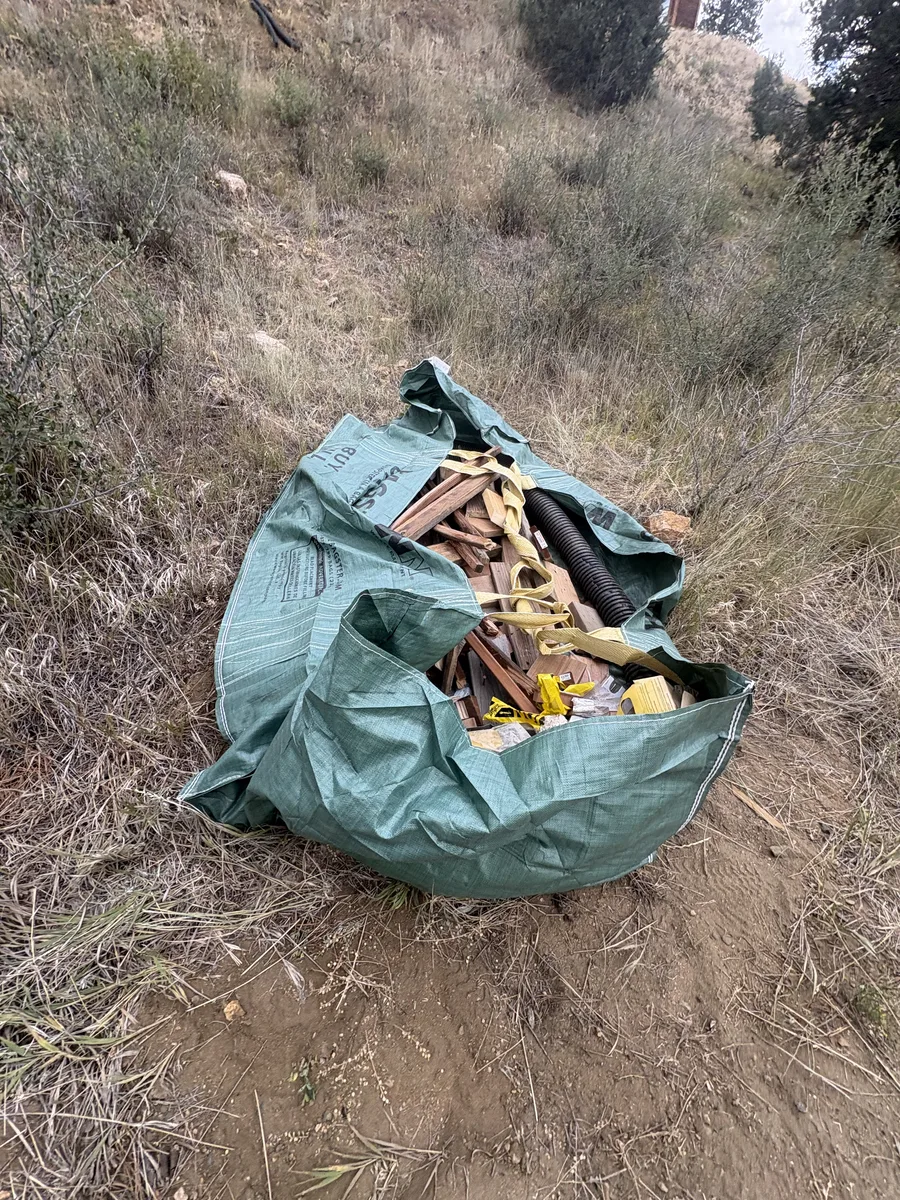 A full Bagster bag of deck lumber debris sitting on a dry hillside in Evergreen, Colorado
